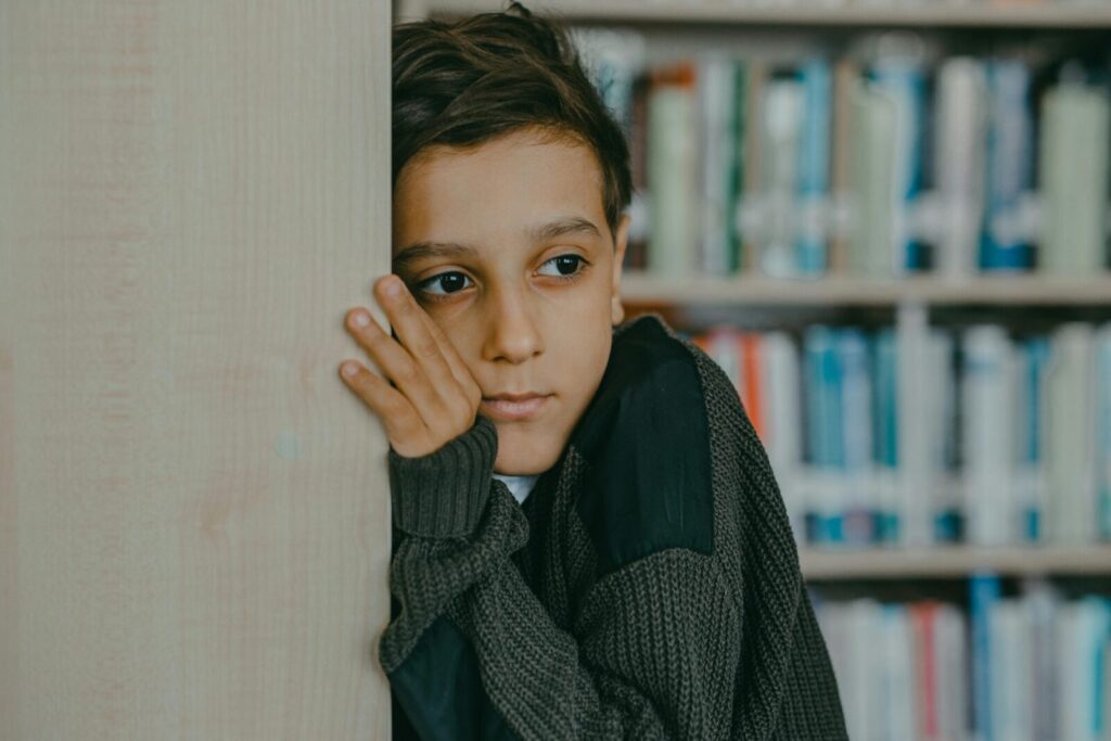 A contemplative child leans against a wall in a library, deep in thought.