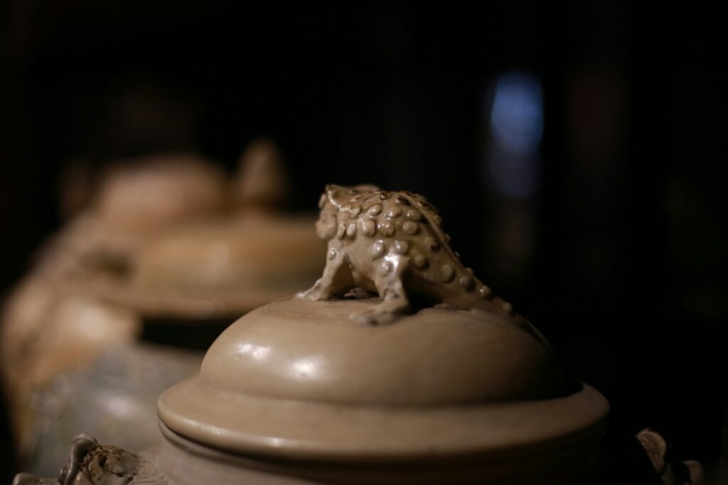 A decorative frog sits atop a ceramic lid.