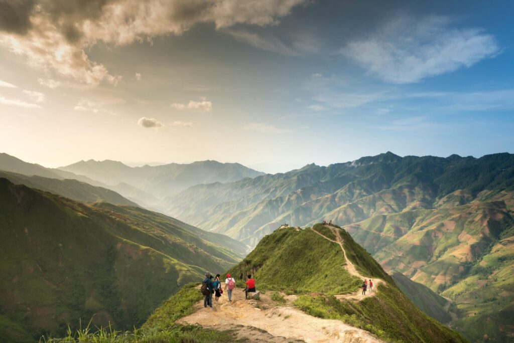 Hikers walking along a scenic mountain trail with a stunning valley view under clear skies.