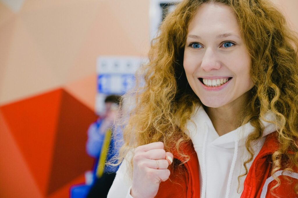Gleeful sportswoman with curly hair in sportswear cheering for team with clenched fists and looking away while standing in arena during curling game