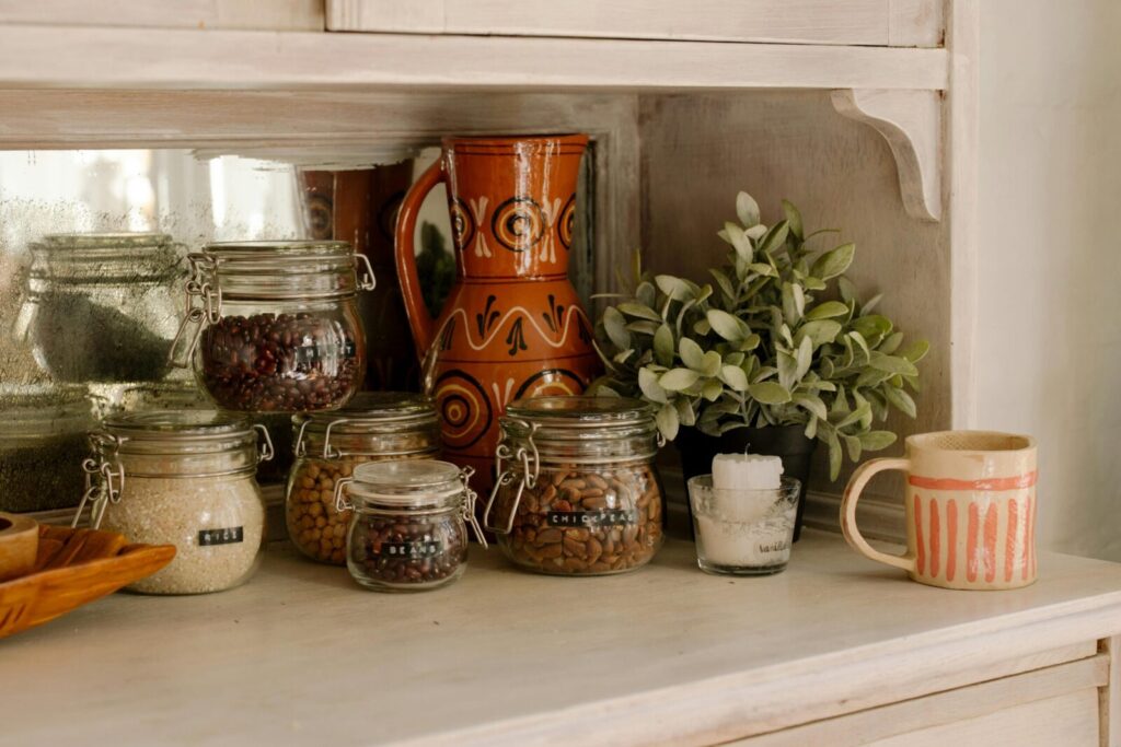 A charming rustic kitchen shelf displaying jars filled with grains and legumes, a decorative jug, and a mug.