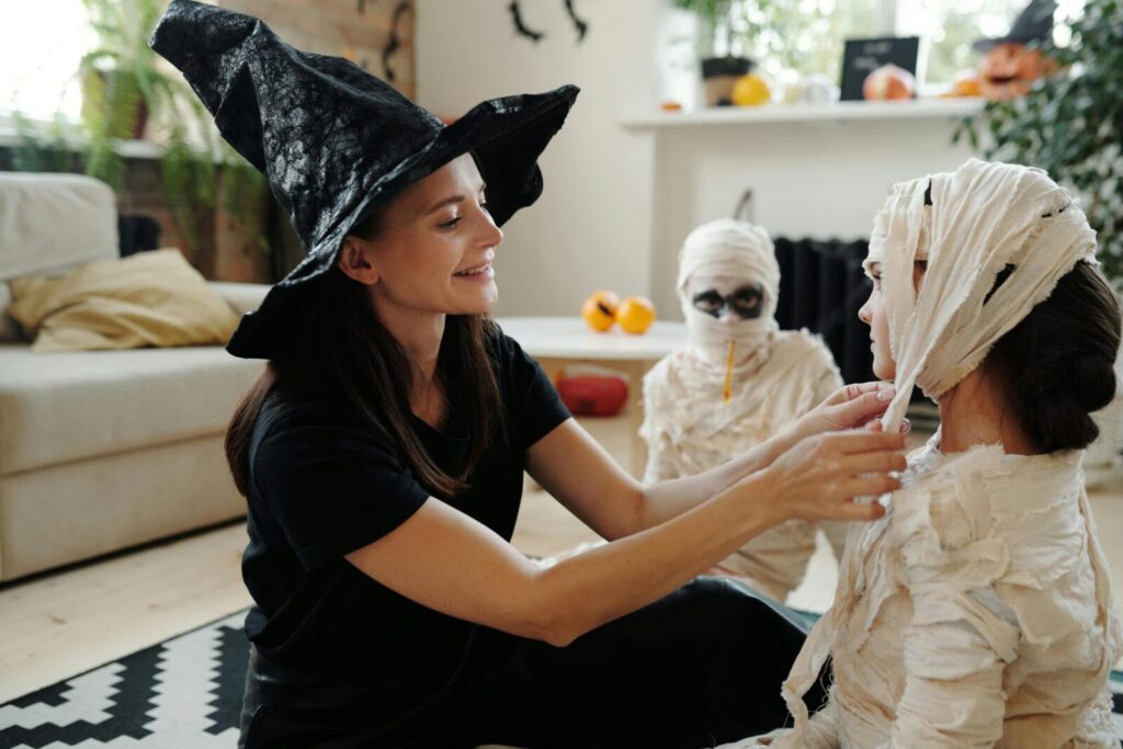 A mother helps her kids dress as mummies for Halloween indoors, fostering fun and creativity.