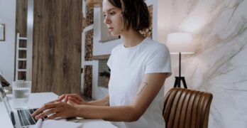Young woman with short hair works remotely on laptop at stylish home office, featuring modern decor and natural light.