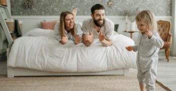 A joyful morning with parents encouraging their young child in a cozy bedroom setting.