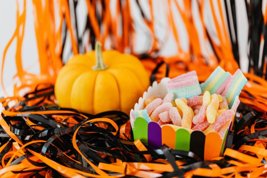 Colorful candies in a vibrant box next to a small pumpkin surrounded by Halloween-themed decorations.