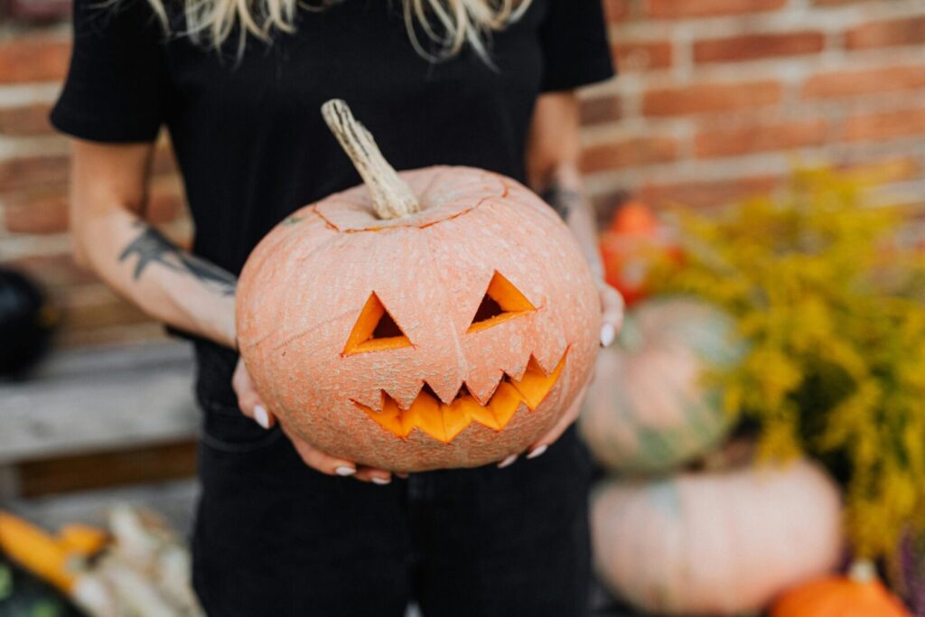 Close-up of a woman holding a carved jack-o'-lantern pumpkin outdoors, embracing Halloween spirit.