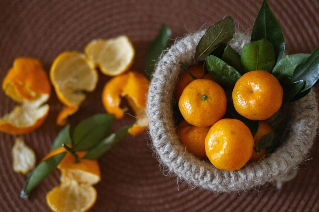 Vibrant mandarin oranges with leaves in a rustic basket, surrounded by peels.