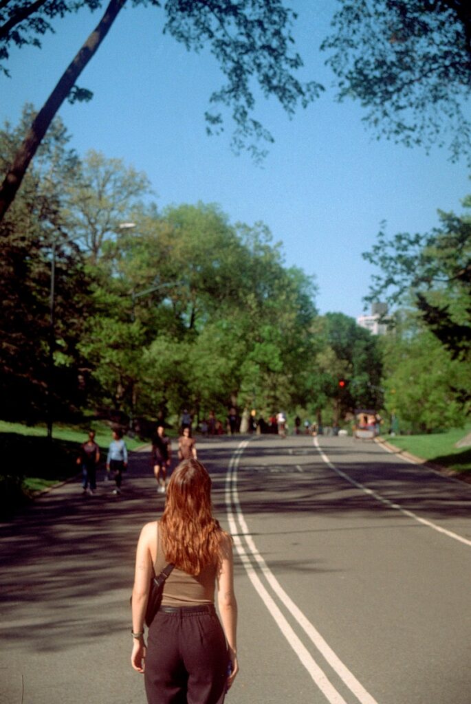 Woman walking on a park road with trees and people.