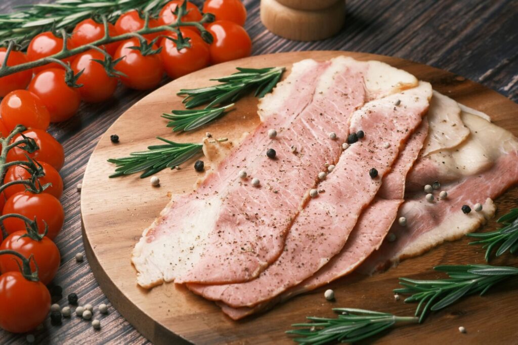 Rustic ham slices with rosemary and cherry tomatoes on wooden board. Perfect for food photography.