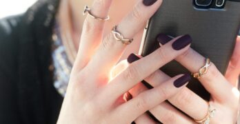 Close-up of a woman with manicured nails and rings holding a smartphone, showcasing fashion elegance.