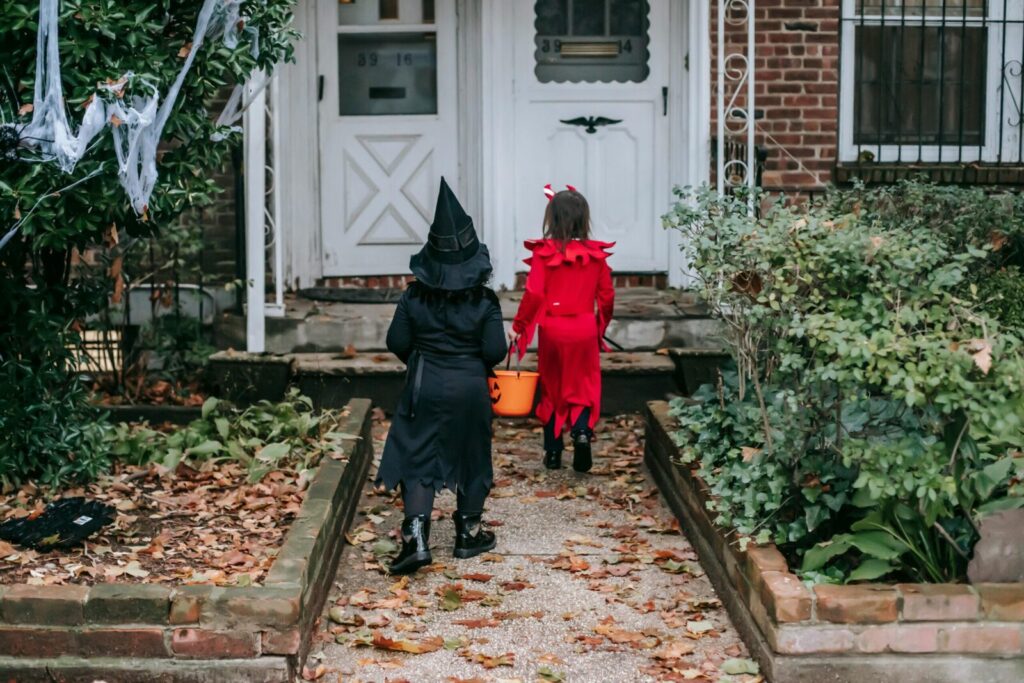 Back view of little children in traditional Halloween costumes going to front doors of semi detached red brick house playing trick or treat custom