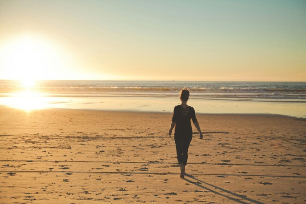 A woman strolls along a sandy beach during a beautiful golden sunset.