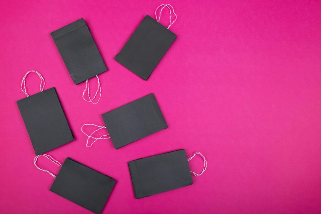 Flat lay of black paper bags arranged on a bright pink background, perfect for shopping concept visuals.
