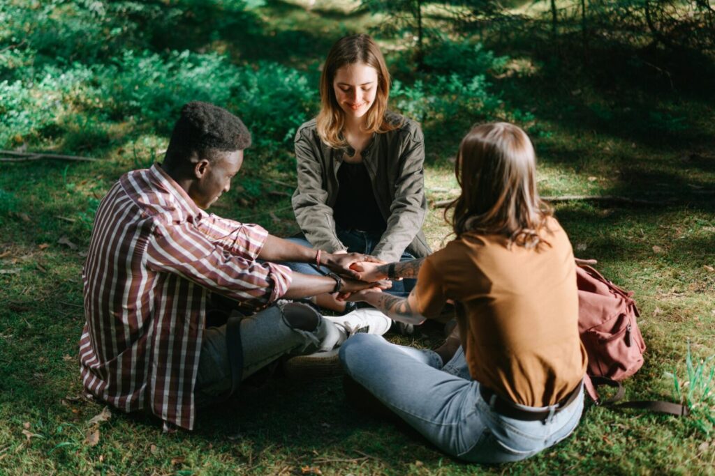 Three friends sitting in a forest, holding hands in a circle, promoting unity and friendship.