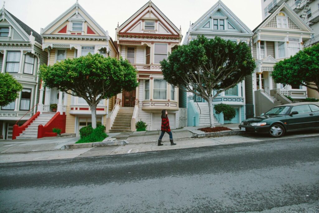 A woman walks past iconic Victorian houses in San Francisco, showcasing urban charm.