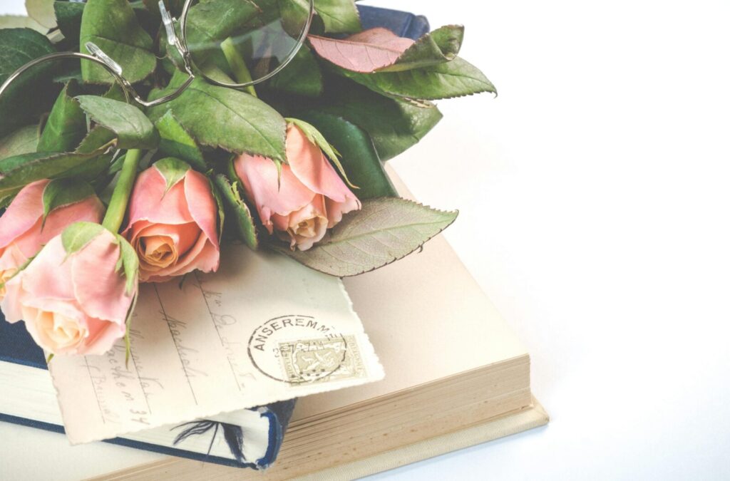 A sophisticated arrangement of pink roses, vintage books, and eyeglasses exuding a classic and serene atmosphere.