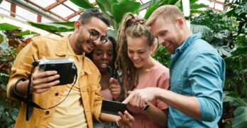 A diverse group of friends having fun with photography inside a vibrant greenhouse.
