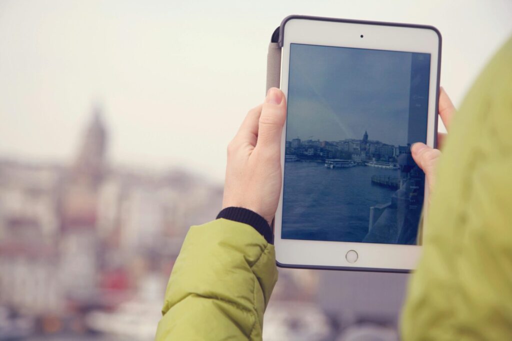 Hands holding a tablet capturing a cityscape, focusing on technology and urban exploration.