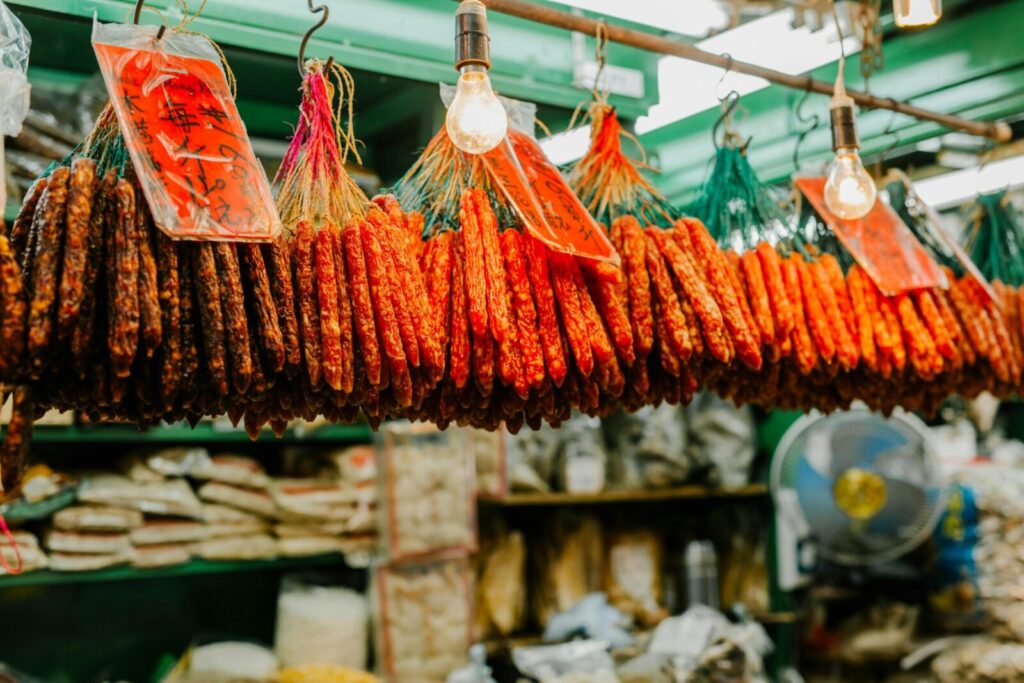 A display of assorted cured sausages hanging in a market stall illuminated by light bulbs.