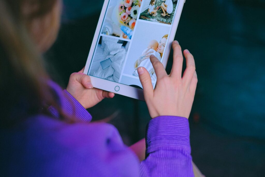 A woman in a purple sweater browsing a digital photo album on a tablet indoors.