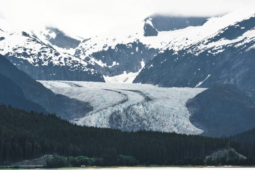 A breathtaking view of an Alaskan glacier surrounded by snowcapped mountains and lush forests.
