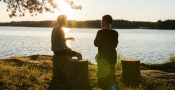man in black jacket standing beside body of water during sunset