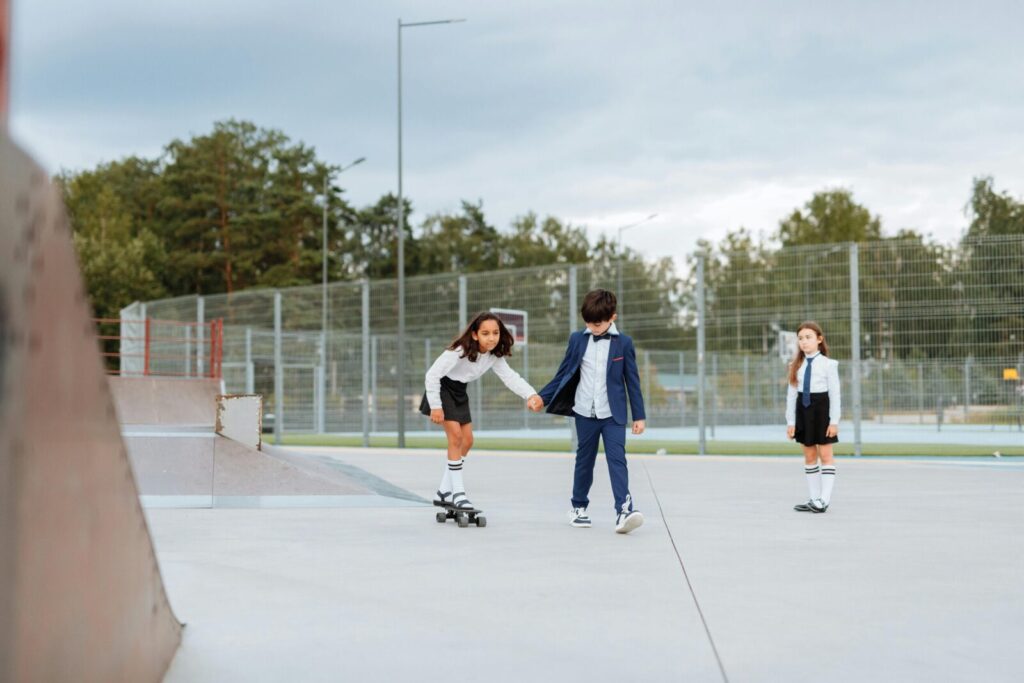 Three children playfully skateboarding together in an outdoor urban park.