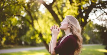 woman praying under tree during daytime