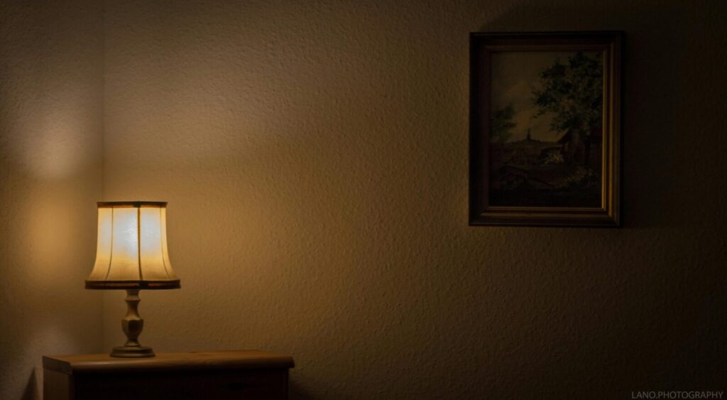 Warmly lit room with a vintage lamp and framed painting on the wall.