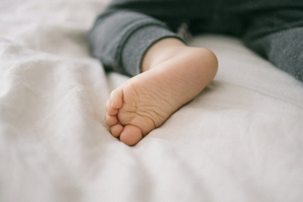 person in gray long sleeve shirt lying on white bed