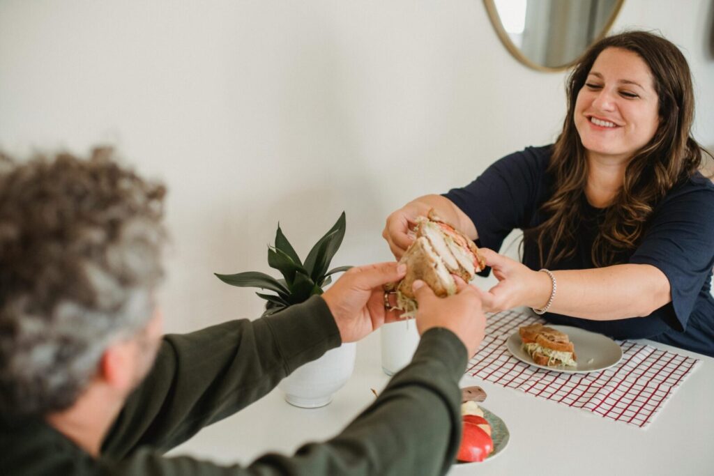 A happy couple enjoying sandwiches at home, sharing a moment of joy and companionship.
