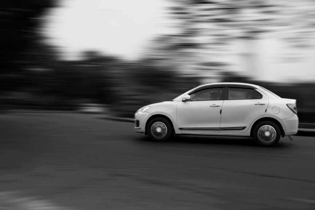 A white car driving down a street next to a forest