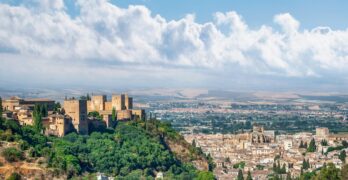A scenic view of the historic Alhambra in Granada, Spain, surrounded by lush greenery and an expansive cityscape.