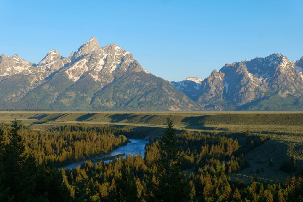 Experience the stunning Grand Teton mountains with vibrant greenery and a serene river at sunrise in Wyoming.