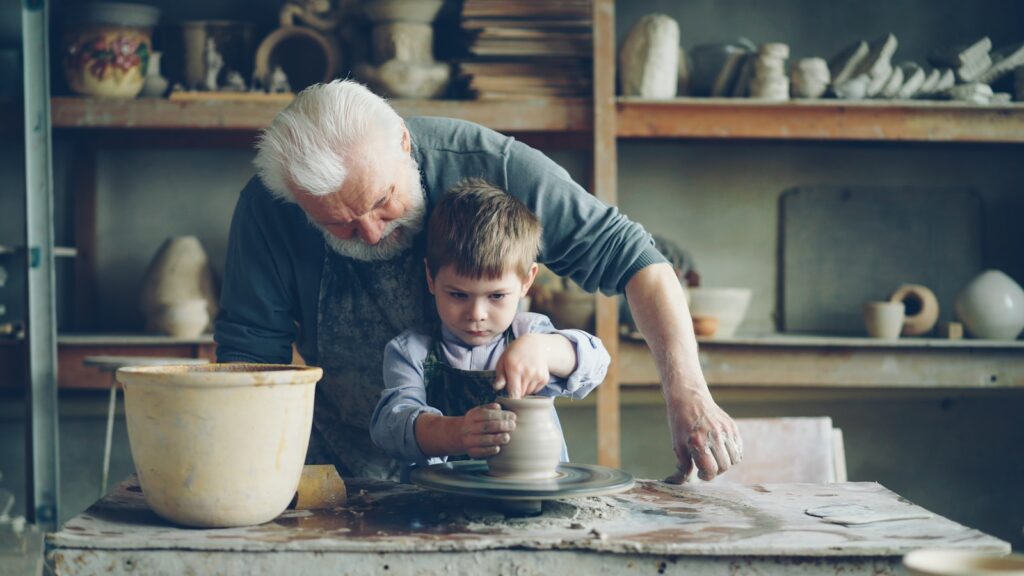 A grandfather teaches his grandson pottery.