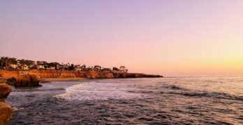 A tranquil sunset view of the San Diego coastline with calm waves and vibrant skies.