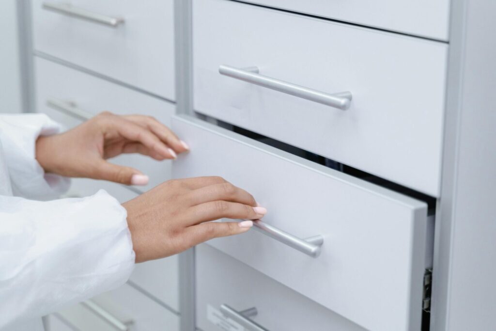 Close-up of hands opening a white drawer, wearing a lab coat in an office environment.