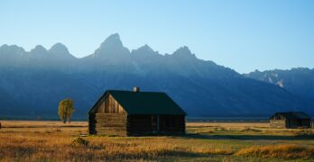A small cabin in a field with mountains in the background