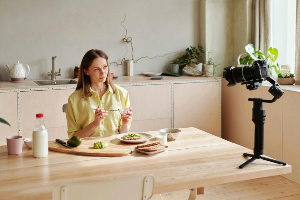 Woman recording a healthy breakfast vlog in a modern kitchen setting, featuring avocados.