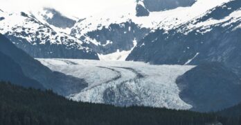 A breathtaking view of an Alaskan glacier surrounded by snowcapped mountains and lush forests.