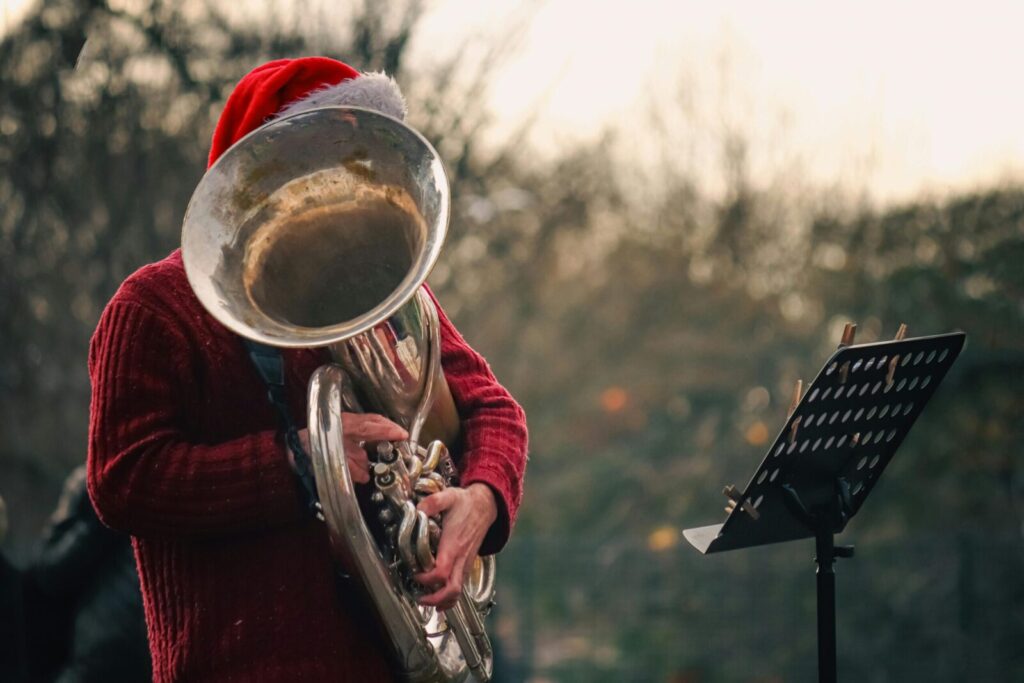 Musician in Santa hat performs on tuba outdoors, creating a festive atmosphere.