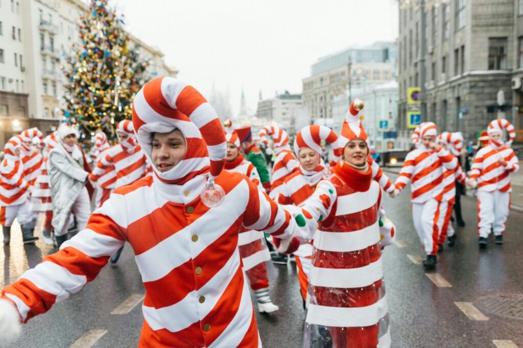 People in candy cane costumes participate in a joyful holiday street parade.
