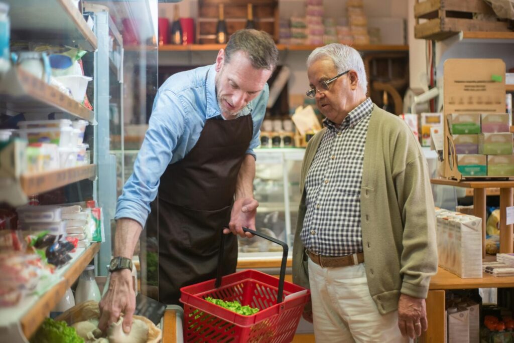 A salesman helps an elderly man with shopping in a local grocery store.