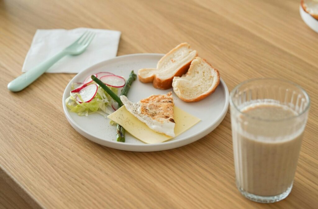 A nutritious breakfast featuring eggs, radish salad, bread, and a smoothie on a wooden table.
