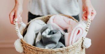 Close-up of hands holding a woven basket full of soft baby blankets indoors.