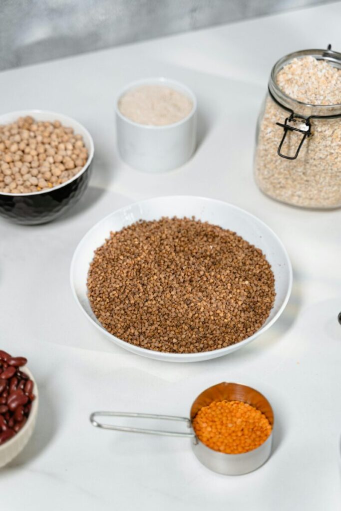 Flat lay of various grains and legumes, including buckwheat, oats, chickpeas, and lentils, on a white surface.
