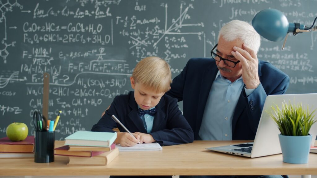 Teacher helping young student with math problems at desk.