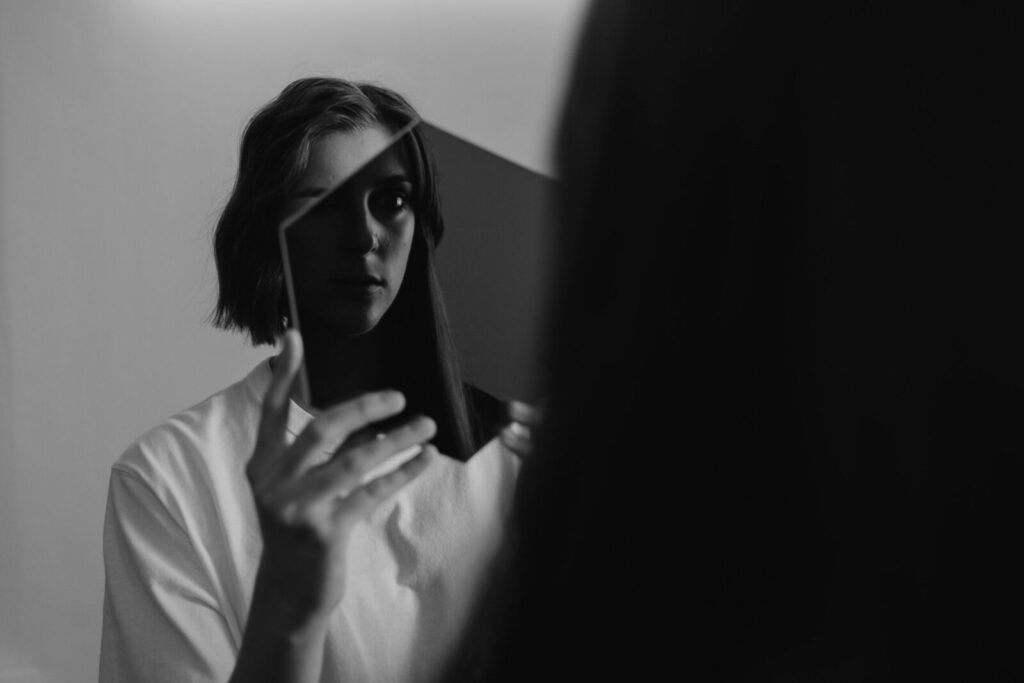Monochrome image of a woman reflecting on herself in a mirror, evoking introspection.
