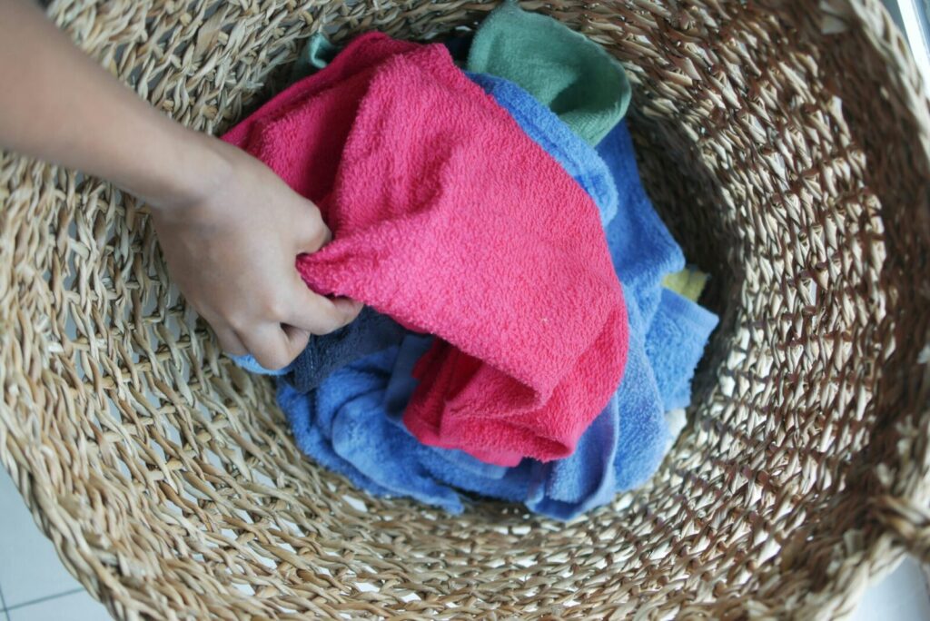 A hand reaches into a wicker basket filled with vibrant colored towels.