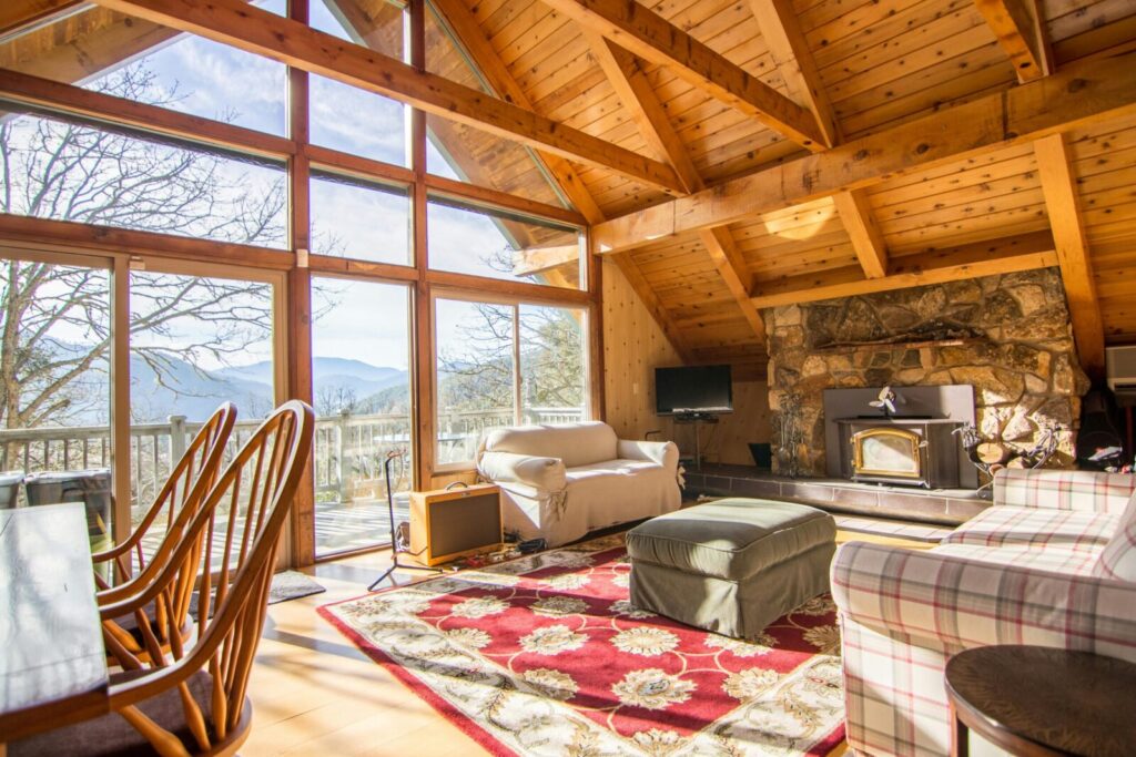 Rustic cabin living room with large windows and scenic views, highlighting wooden interiors.